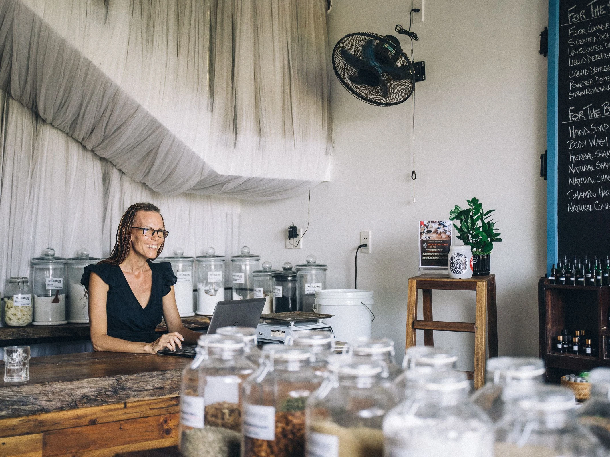 A shop owner using a laptop inside a store that sells goods