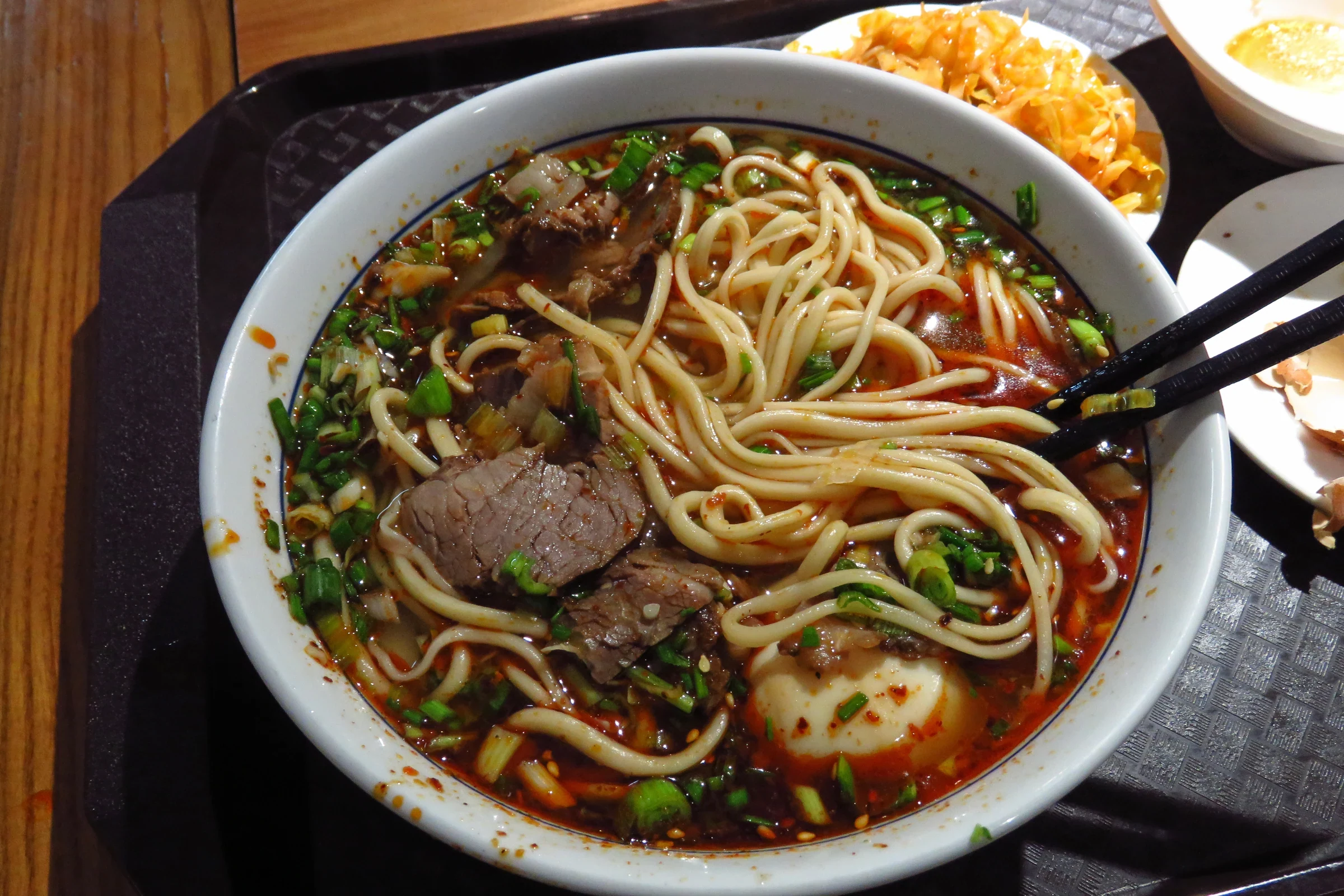 Lanzhou beef noodles with noodles, beef, and egg in the bowl, plus side dishes