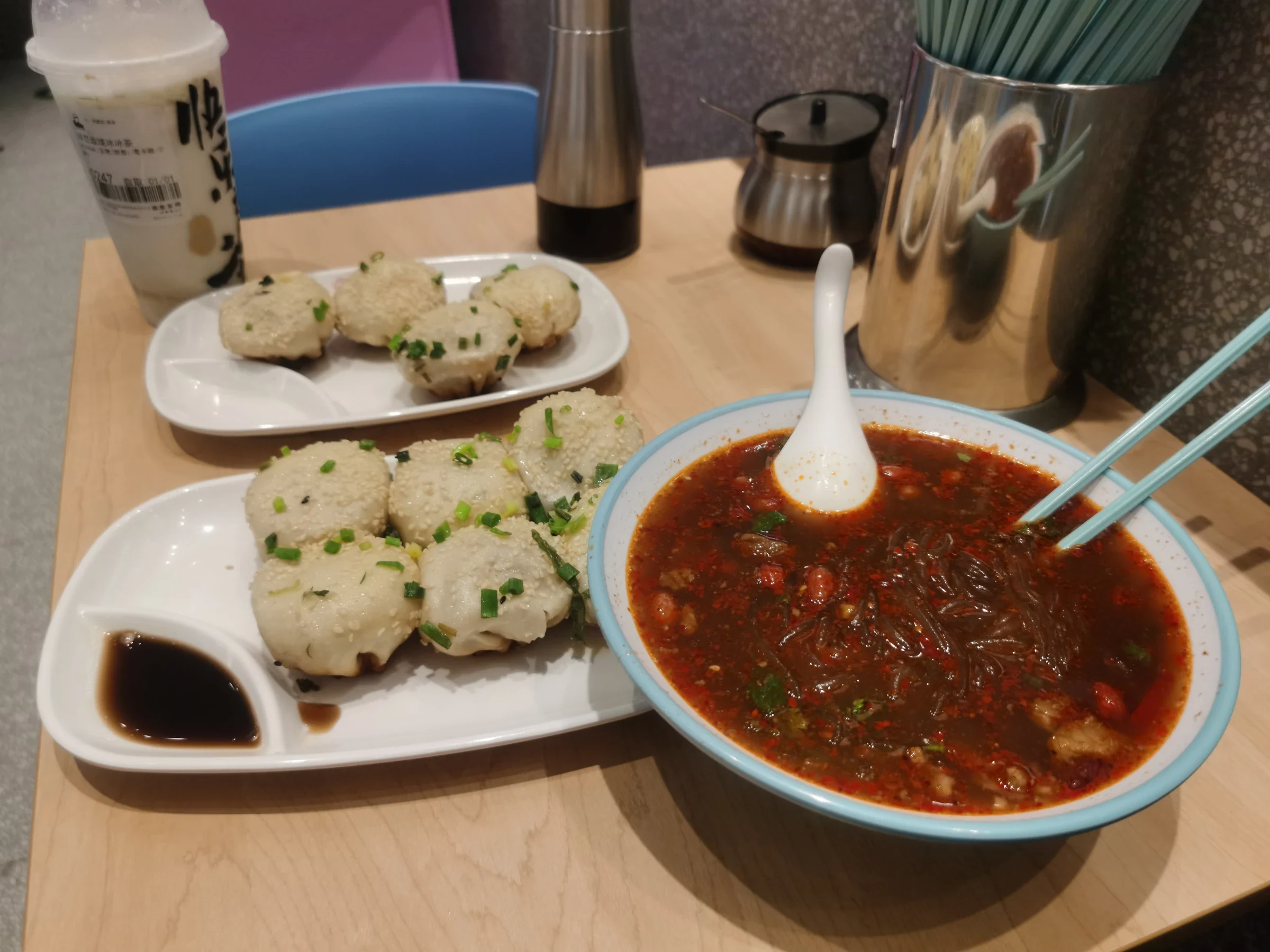Shengjian buns and hot-and-sour noodles on a table at Suzhou Center, with a drink beside them