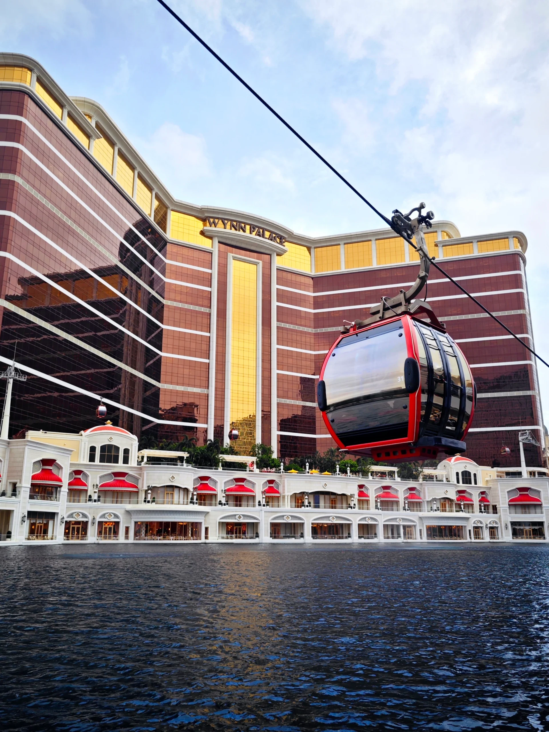 Red cable car cabin above the Wynn Palace Performance Lake by day in August 2025